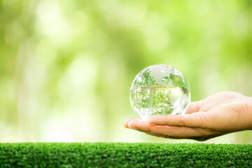 Human hand holding globe planet glass In green forest with bokeh nature lights. world environment...