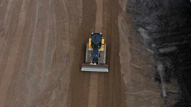 Drone shot following yellow bulldozer reversing through graded sand leaving behind tracks
