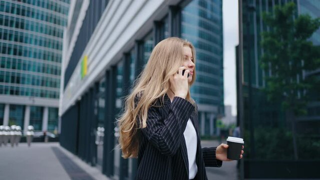 businesswoman is talking by cell phone while walking in city center in modern business district