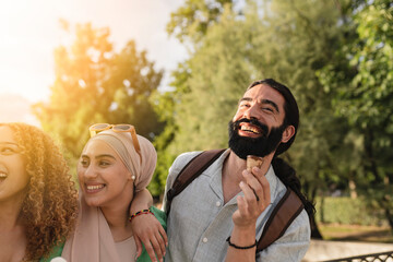 Obraz premium Multiracial friends eating ice cream in the park and having fun, focus on bearded man.