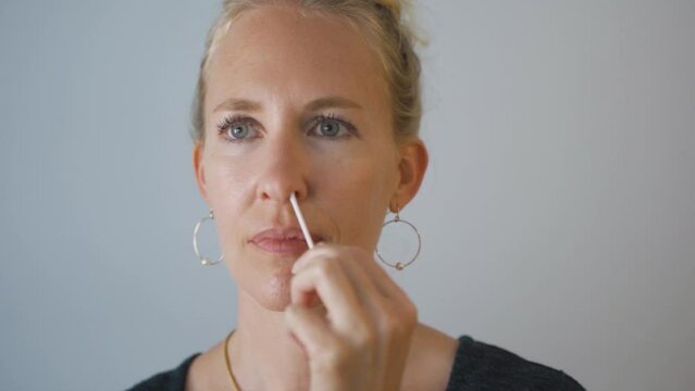 Blonde woman at home performing a nasal PCR self-test for Covid-19