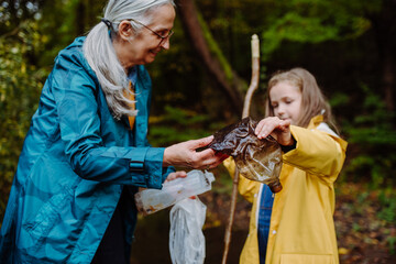 Small girl with grandmother showing plastic waste what they found outoors in forest.