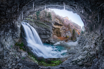 Waterfall behind cave in nature