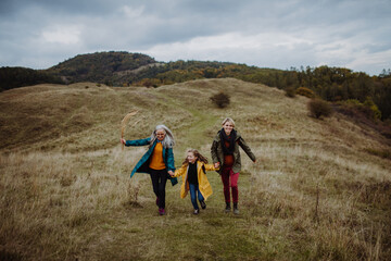 Happy small girl with mother and grandmother hiking outoors in autumn nature.