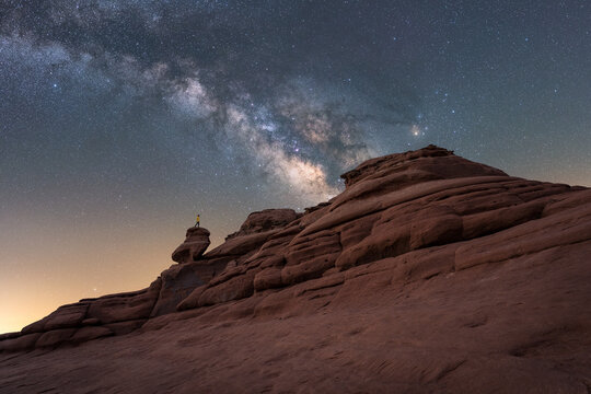 Tourist standing on stone formation under starry sky with Milky Way
