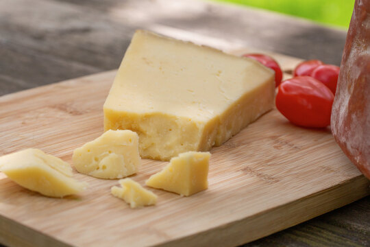 Piece of Italian cheese with cherry tomatoes on cutting board in countryside