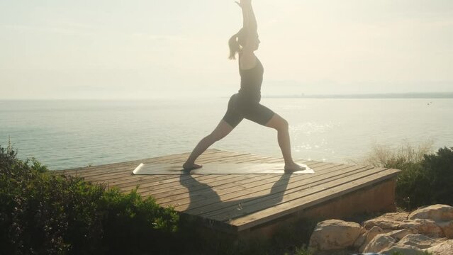 A young woman practices yoga on the background of the sea, on a summer day