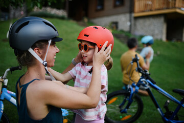 Young mother with little daughter preaparing for bike ride, putting on helmets.