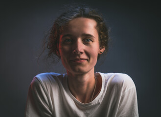 Young thin girl like a boy in a white t-shirt look straight smiling portrait on a gray background baby face girl looks like a boy tanned face