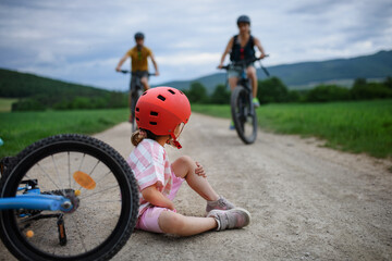 Mother and father rushing to help their little daughter after falling off bicycle outdoors