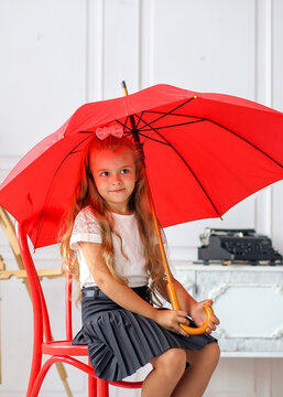 Cute little schoolgirl sitting with a red umbrella on a chair in a room where: table, chair, abacus, books, backpack. Offline and online. Education concept