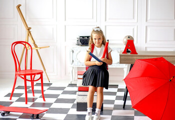 Cute caucasian schoolgirl having fun with big pencils in a room where: table, chair, abacus, books, red umbrella, backpack. Soon to school. education concept