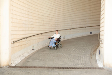 Fototapeta na wymiar a woman with sunglasses sitting in an electric wheelchair going down an urban ramp. Concept of a handicapped accessible city