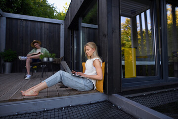 Happy young couple with laptop resting outdoors in a tiny house, weekend away and remote office...