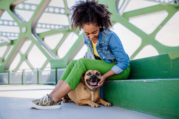 Multiracial girl sitting and resting with her dog outside in the bridge, training him, spending leisure time together. Concept of relationship between dog and teenager, everyday life with pet.