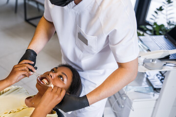 Woman fixing transparent tray at the mouth while doctor preparing to the whitening procedure