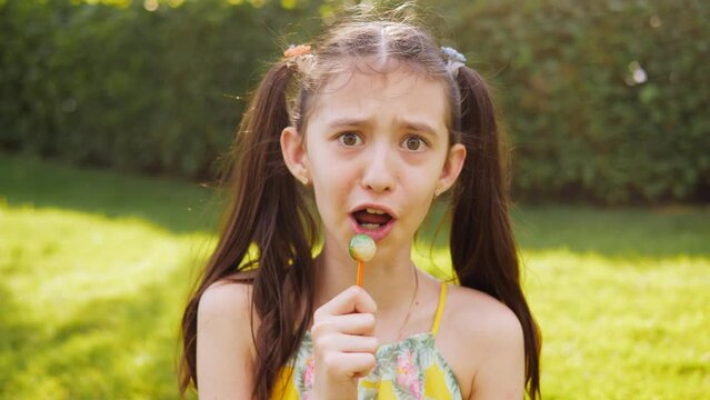 A preteen girl in the park licks a lollipop laughs and monkeys on camera