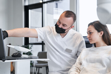 Obraz premium Calm woman looking at the laptop screen while doctor explaining to her steps of teeth whitening