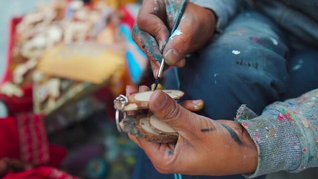 Close up shot of street painter hands painting wooden keychain on the street of Mall Road Manali, Himachal Pradesh, India. Urban lifestyle, street art concept.   street artist - painter
