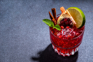 Spicy autumn pomegranate cocktail. Alcohol warming gin drink with pomegranate, lime, cinnamon, mint, autumn winter sangria on dark background copy space