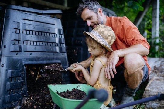 Father with his daughter putting compost out of composter, farmer lifestyle.