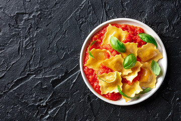 A plate of ravioli with tomato sauce and basil, simple Italian meal, shot from above on a black background with a place for text