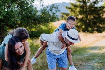 Happy parents giving their children piggyback ride in summer in nature.