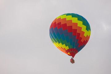 Fototapeta premium Colorful rainbow hot air balloon flying against grey sky at Winter aerostat festival. Freedom, sport, aircraft concept