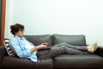 Young Caucasian Man work from home on laptop and connect online to office indoor for remote internet workplace. Young Adult male  is freelance work smart on notebook lying on sofa couch, copy space