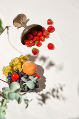 Summer background with fruits, berries and wine glass on white table. Light background with shadows from wine glasses and fruit with copy space. Summer food backdrop with empty place. Summer menu.