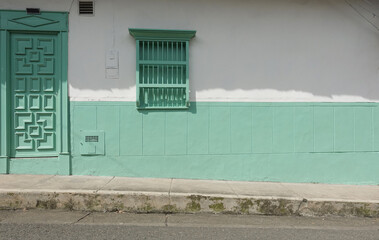 mint colored facade of a traditional house in a small colombian town with sidewalk. the wooden door...