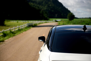 Close-up rear view of a white car with mountains and sky on the road.