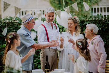 Mature bride and groom toasting with family at wedding reception outside in the backyard. Vow...
