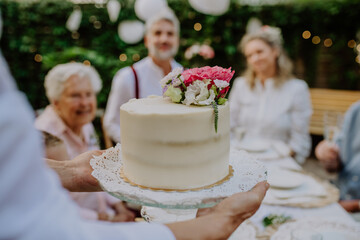 Mature bride and groom getting a cake at wedding reception outside in the backyard.