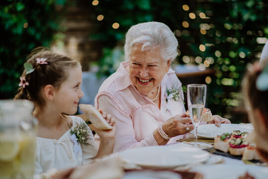 Wedding guests sitting by table, eating and drinking at reception outside in the backyard. Grandmother and granddaughter talking each other.  - Powered by Adobe