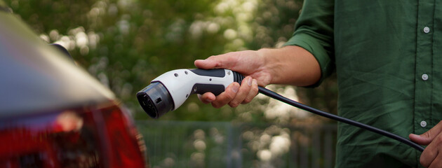 Man holding power supply cable at electric vehicle charging station, closeup