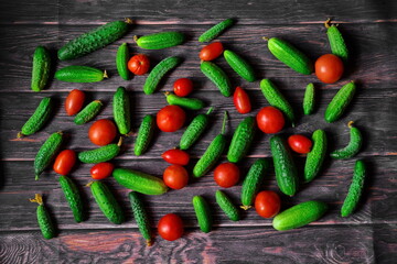 Vegetable background. Pattern of green cucumbers and red ripe tomatoes of different shapes and sizes laid out on wooden boards. Top view, flat lay