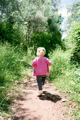 Little girl walks along the path in the park, raising her legs high. Back view. High quality photo