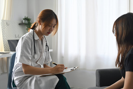 Asian female doctor consults patient and filling documant form.