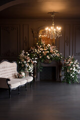 Black room interior with a vintage sofa, chandelier, mirror and fireplace decorated with flowers