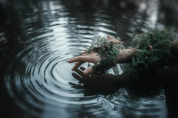 In harmony with nature. Hand covered with moss fingers touch the surface of the water. Man and...