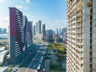 Drone view of an almost completed residential multi-storey building with a tower crane overlooking the city street on a sunny day. Multi-storey residential building is being built using a crane.