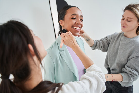 Multiracial woman smiling with pleasure face while team of professionals working on her look