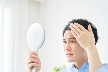 自宅でハンドミラーを持って髪の毛を見る男性