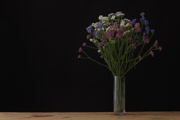 dried flowers of different colors, statice in a glass vase on a wooden table, dark background, mockup