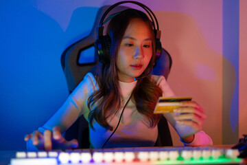 Top up online game with credit card concept. Gamer and E-Sport online of Asian woman playing online computer video game with lighting effect, broadcast streaming live at home. Gamer and E-Sport gaming