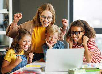 Teacher and cheerful  schoolkids   looking at laptop screen and celebrate   successful completion of collective school work   during online lesson