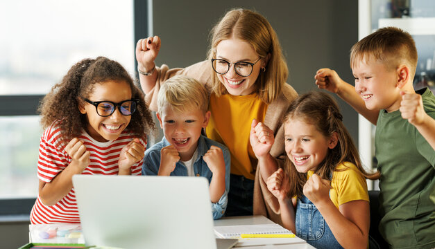 Teacher and cheerful  schoolkids   looking at laptop screen and celebrate   successful completion of collective school work   during online lesson
