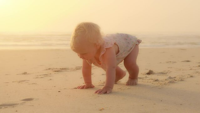 Happy Caucasian little baby crawl alone on knees outdoors on sand seaside coast. Infant small girl boy daughter toddler child kid learns crawling quickly learning walks on beach near ocean on vacation