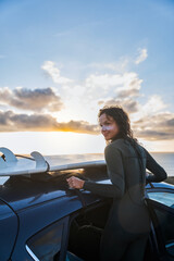 Vertical shot of the surfer woman unpacking board from a car's roof rack at the nature